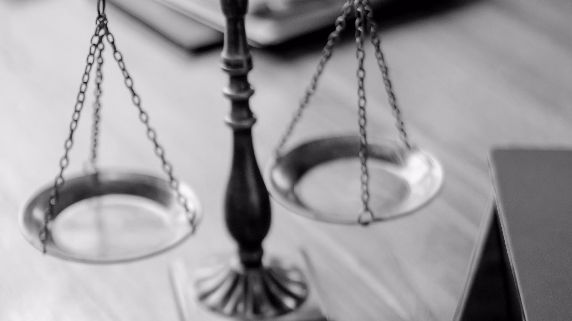 Brass scales of justice on a wooden desk, in black and white.
