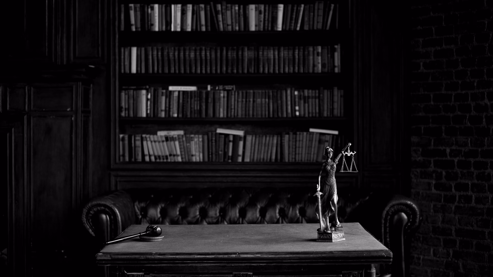 A law study in black and white: shelves of books, a leather sofa and a statue of Lady Justice on the desk.